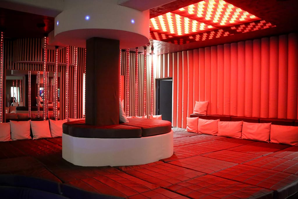 Un salon éclairé en rouge avec des plateformes rondes rembourrées, des coussins et des bandes lumineuses LED verticales dans un espace spa moderne.