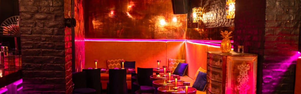 La couverture de @Divine Alcôve montre un lounge tamisé aux murs de pierre, éclairé par des néons rouges et violets, avec banquettes en velours et tables à la bougie.