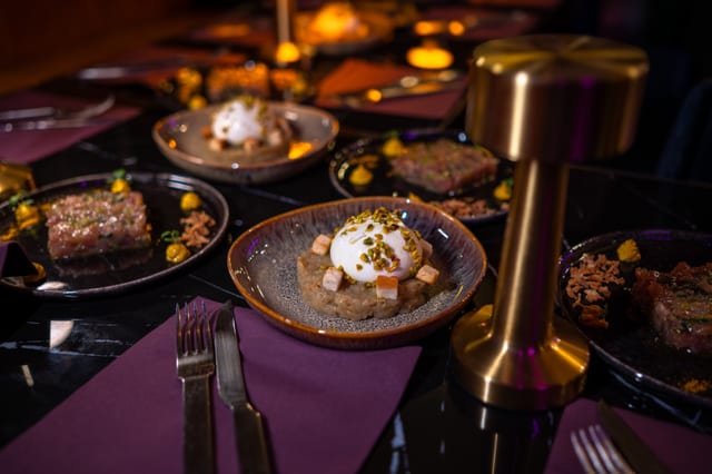 Gros plan sur un dîner dressé avec garnitures gastronomiques sur des sets de table violets, entouré de verres dorés et d’autres plats.