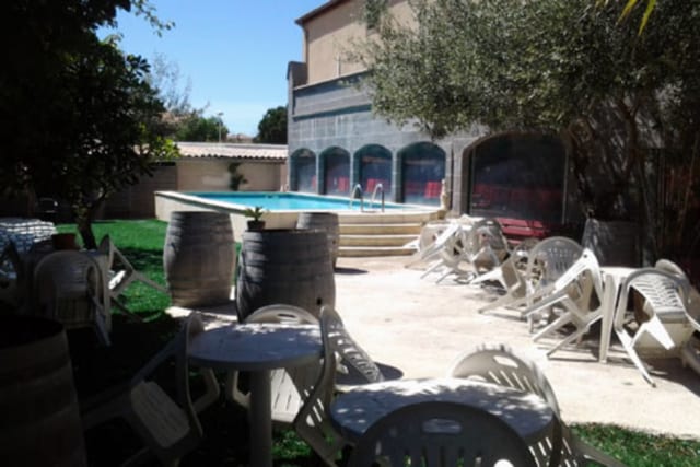 Cour ensoleillée du Château de Trédos avec des fauteuils de terrasse et des jardinières le long de la pelouse, donnant sur la piscine et les ouvertures en pierre voûtées.