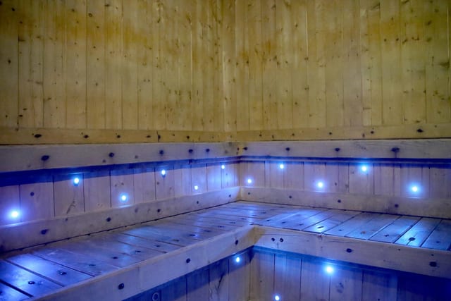 Une piscine intérieure en bois, éclairée par des LED bleues, brille derrière un bord de bassin incurvé dans un décor calme et inspiré du bien-être.