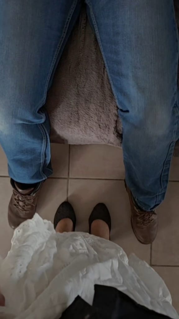 Gros plan sur un jean en denim bleu et des bottes marron posés sur un sol carrelé, avec un tissu blanc étalé au premier plan, dans une lumière douce.